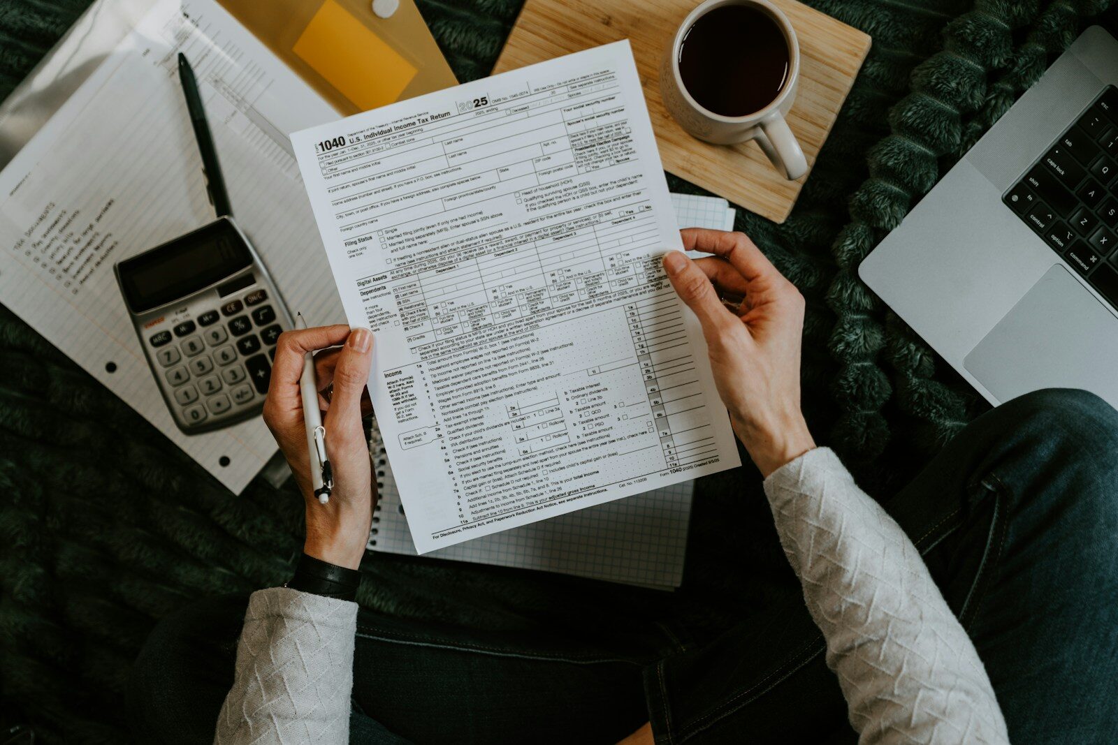 Hands holding tax forms with calculator and laptop.
